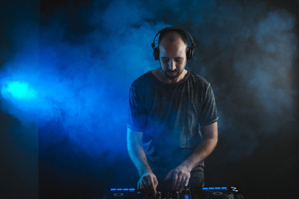 A male DJ working under the blue lights and smoke in a studio against a dark background